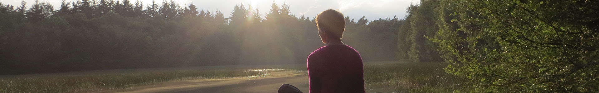persoon in het bos die mindful voor zich uitkijkt met zon op de horizon